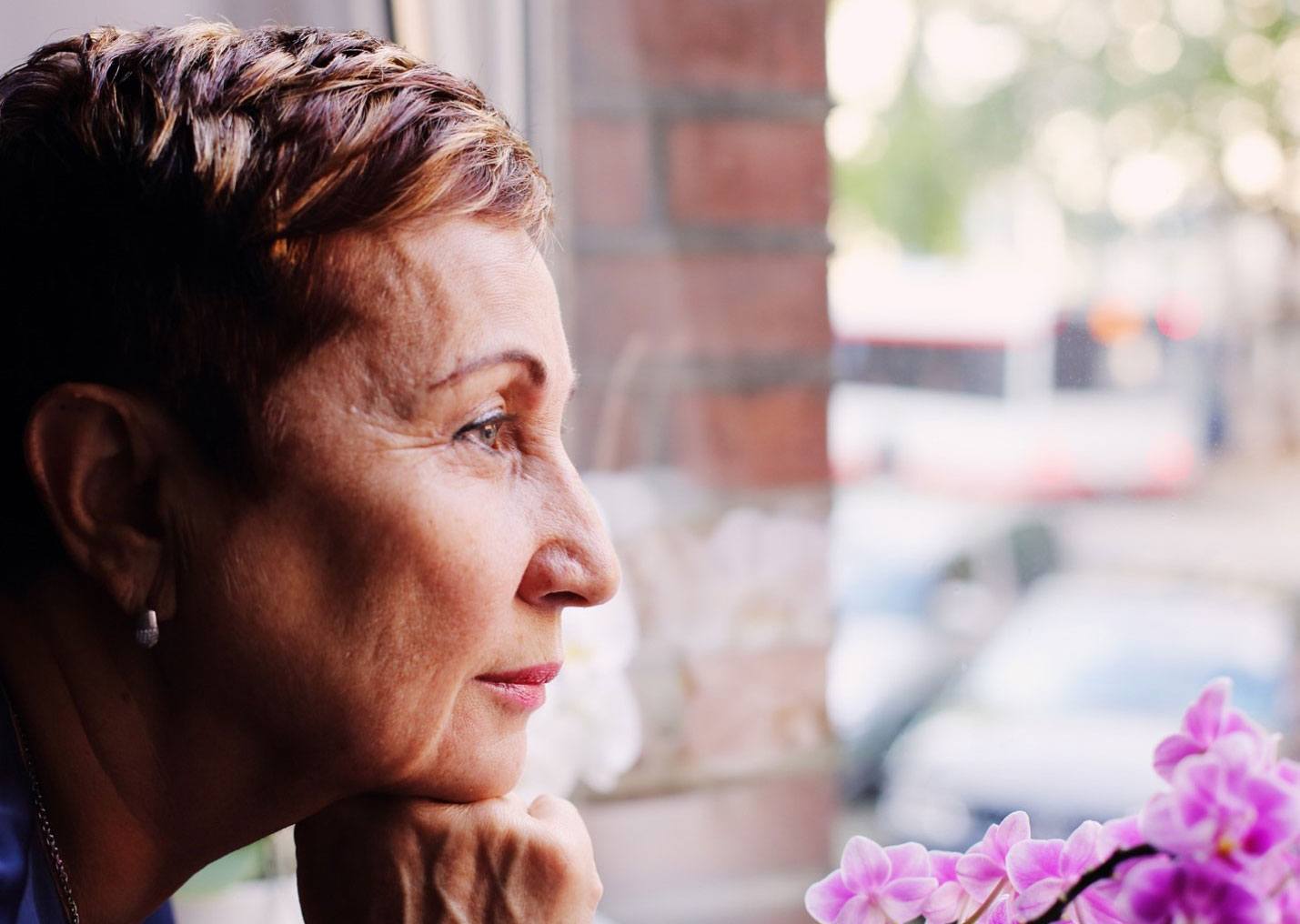 A senior woman looking through window and thinking about retirement plans | Outlook Wealth Advisors